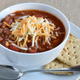 Bowl of chili with cheese on top beside spoon and crackers